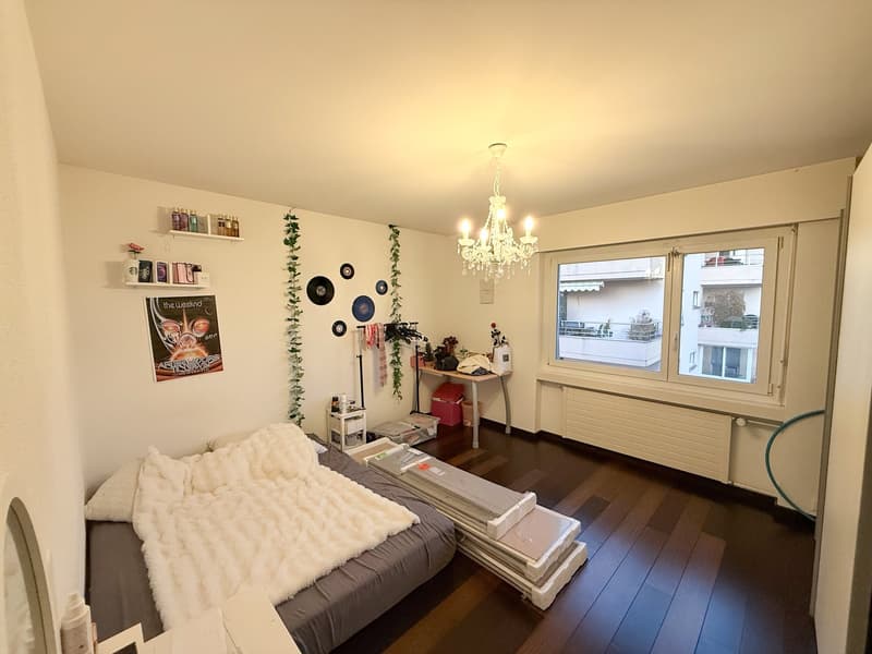 bedroom with a bed, window, chandelier, small table, radiator, wall decorations, storage boxes
