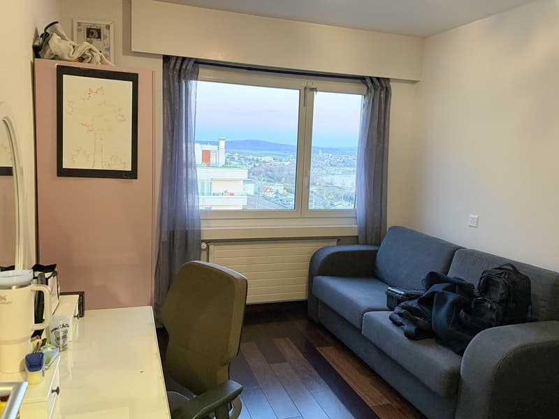 room with a desk, chair, sofa, radiator, window with curtains, framed picture, shelf with items