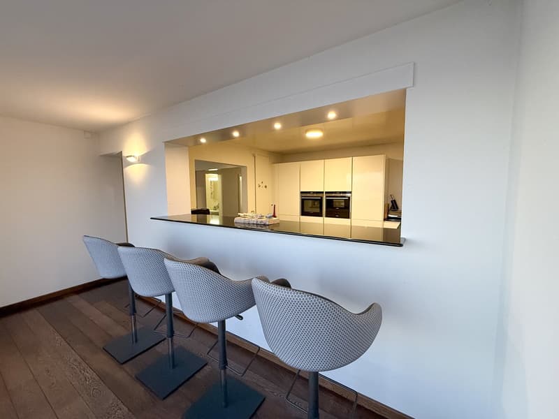 modern kitchen with counter bar, white cabinets, black countertop, four bar stools, built-in ovens, wooden floor