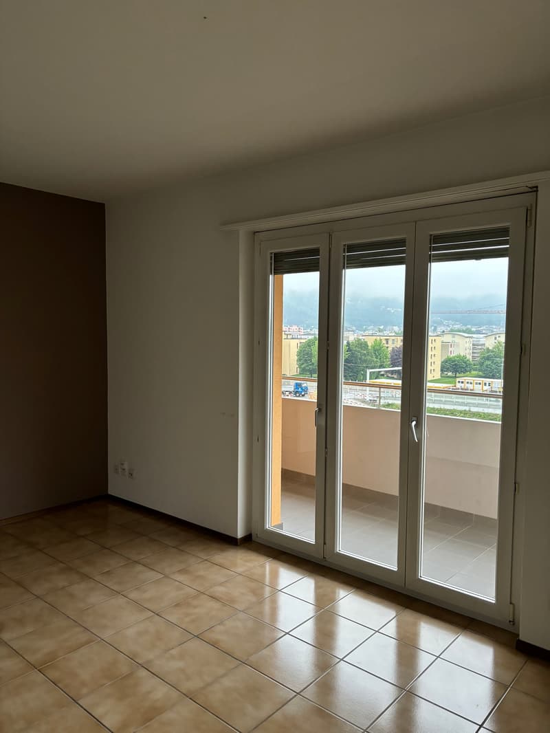Empty room with tiled floor, white walls, and sliding glass doors leading to a balcony with a city view.