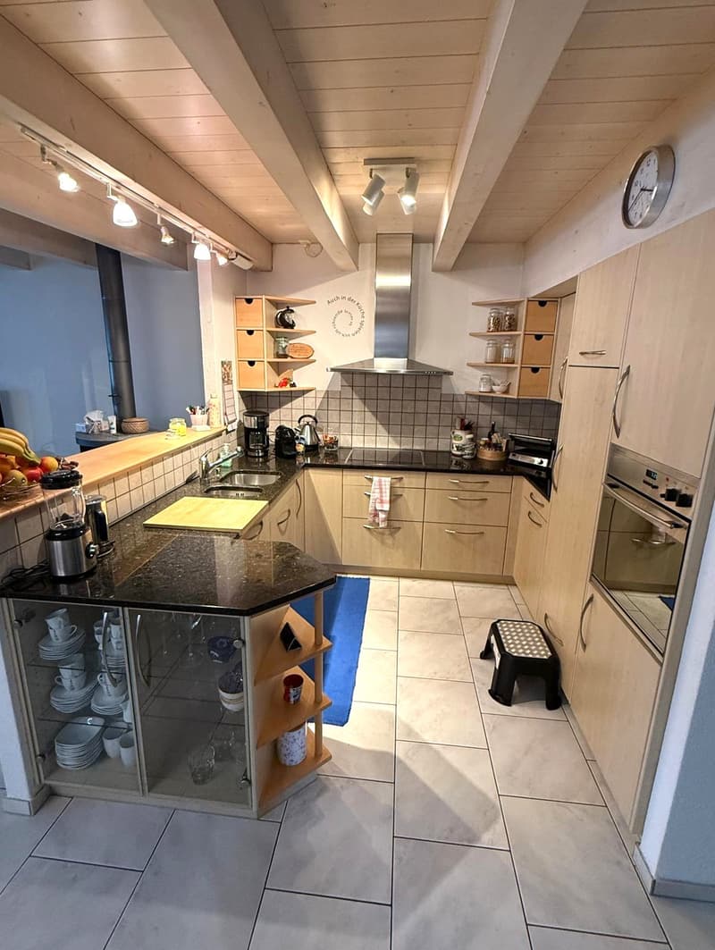 Modern kitchen with wooden cabinets, granite countertop, stainless steel appliances, built-in dishwasher, fridge, stove, extractor hood, wooden shelves, tiled floor, sink with double faucet, decorative elements, stools, decorative plate rack