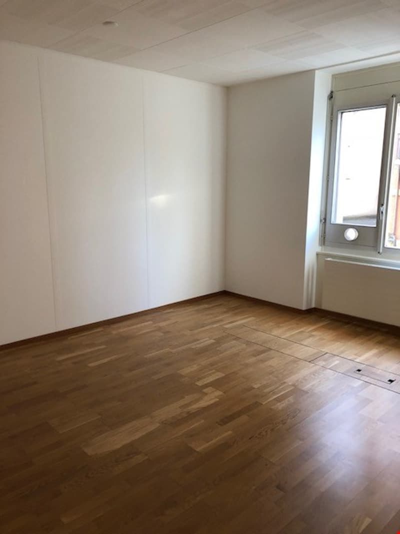Empty room with hardwood floors, white walls, a large window on the right side.