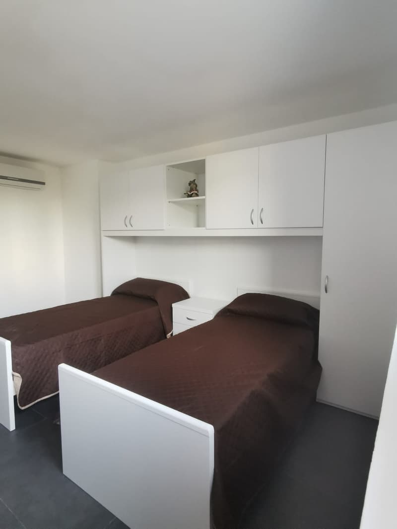 White walls, white built-in cabinets, two twin beds with brown bedding, dark flooring