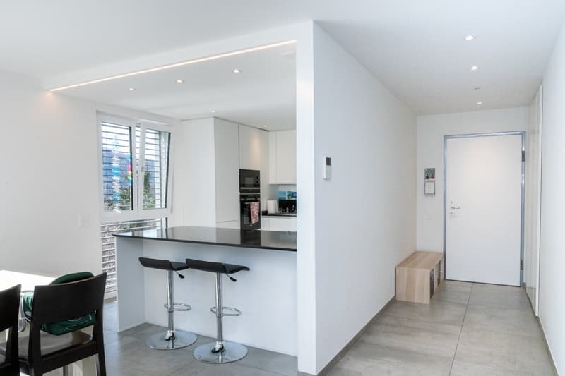 modern kitchen with island, white cabinets, black countertops, two bar stools, white walls, tiled floor, window with blinds
