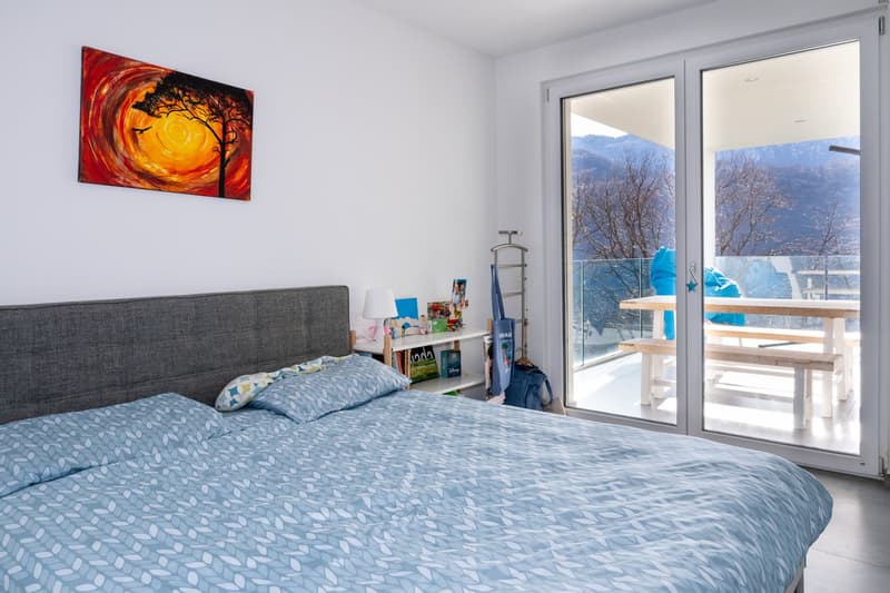 A bedroom with a bed, a nightstand, a painting, and a balcony with a table and benches