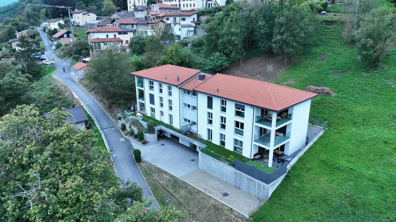 White building with red roof, multiple balconies, underground garage, surrounded by trees and grass