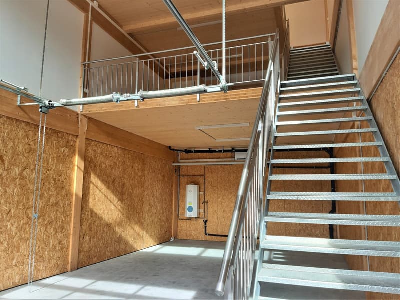 wooden floor, walls made of wood panels, balcony, stairs to balcony, metal railing, pipes and cables attached to the ceiling