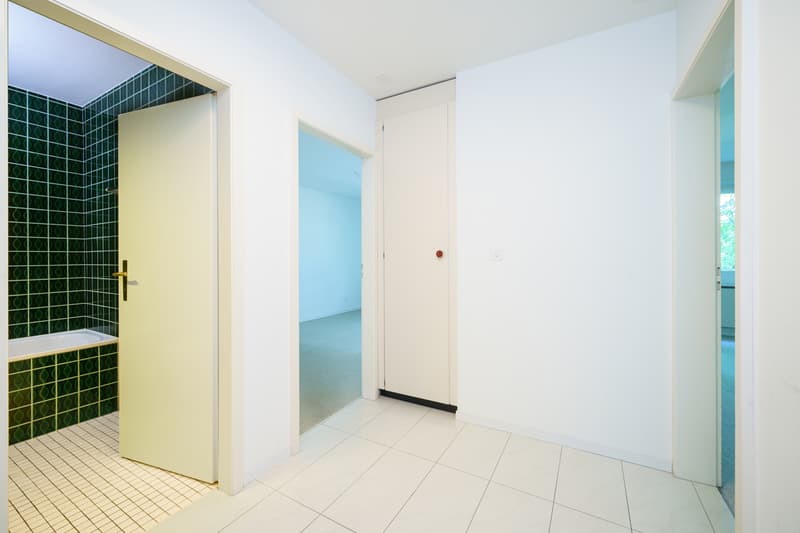 ein Badezimmer mit grünen Fliesen an den Wänden und einer weißen Dusche mit offener Tür / a bathroom with green tile on the walls and a white shower with an open door