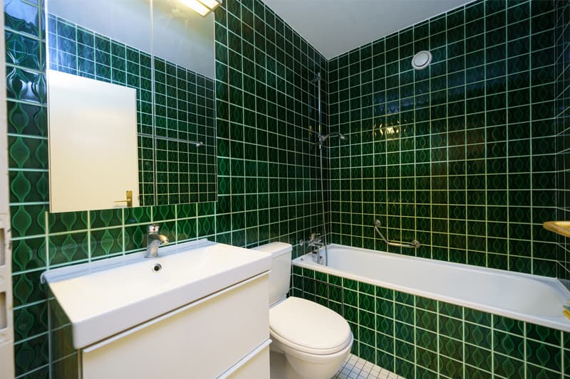 ein Badezimmer mit grünen Fliesen an den Wänden und einem weißen Waschbecken und einer weißen Badewanne / a bathroom with green tiles on the walls and a white sink and bathtub