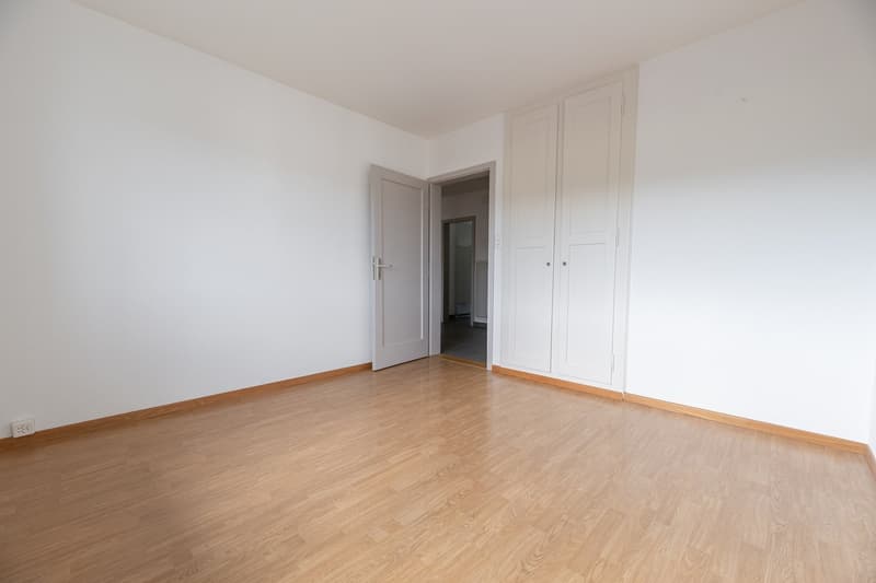 Spacious bedroom with white walls, hardwood flooring, and built-in closets along the wall.