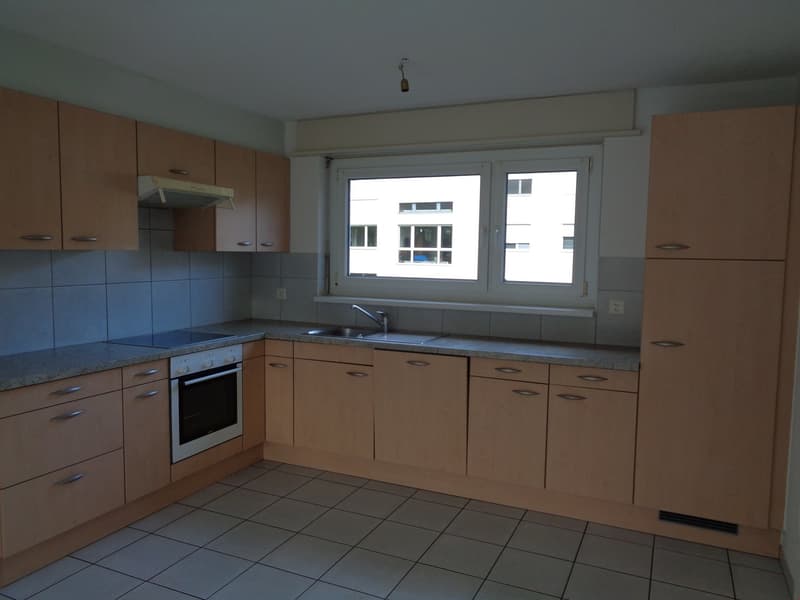 Spacious kitchen with wooden cabinets, blue tile backsplash, built-in oven, and a large window providing natural light