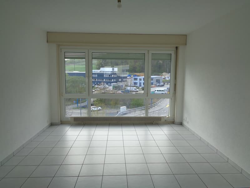 Large room with floor-to-ceiling windows offering a view of the surrounding buildings and landscape. The room has a tiled floor and appears to be empty, ready for furnishing and use.