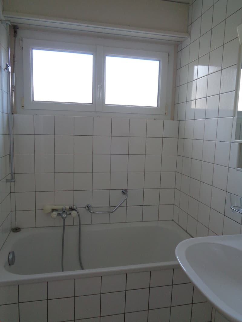 Tiled bathroom with a bathtub, shower fixtures, and a window.