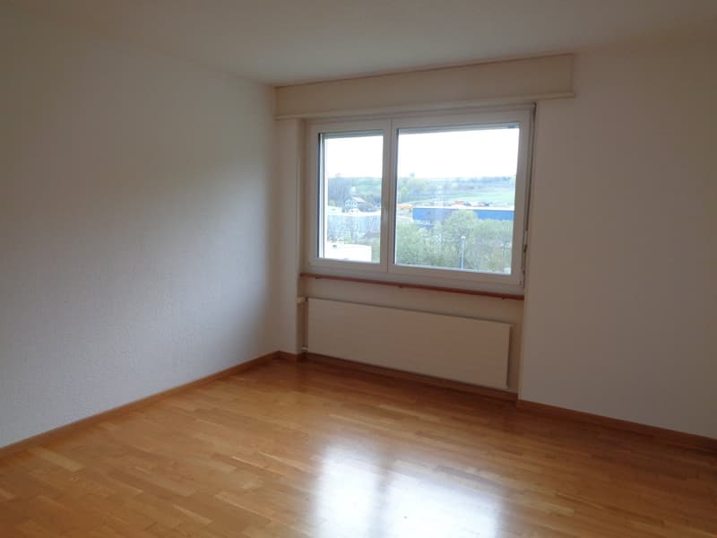 Spacious bedroom with large windows offering a scenic view of the surrounding landscape. The room has hardwood flooring and white walls, providing a clean and bright atmosphere.