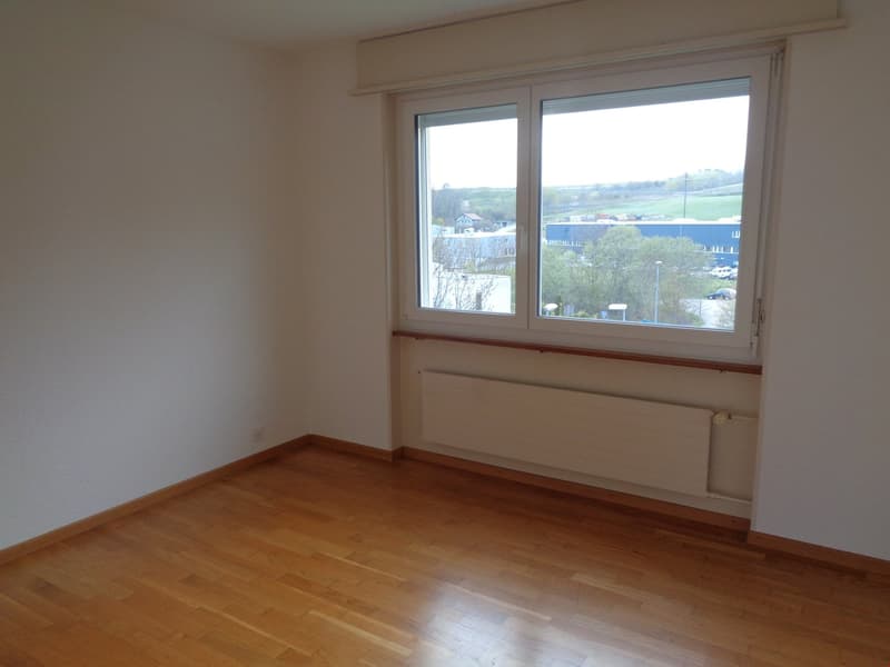 Spacious bedroom with large windows offering a scenic view of the surrounding landscape. The room has hardwood flooring and neutral-colored walls.