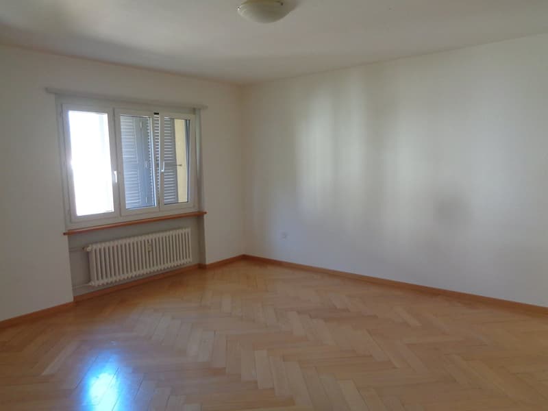 Spacious bedroom with hardwood flooring, white walls, and a radiator. Large windows provide natural light to the room.