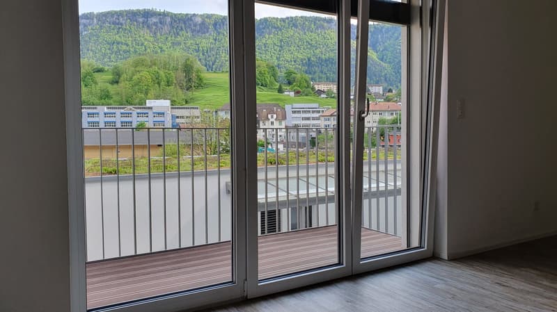 Large windows with a balcony overlooking a scenic landscape of green hills, forests, and buildings in the distance.