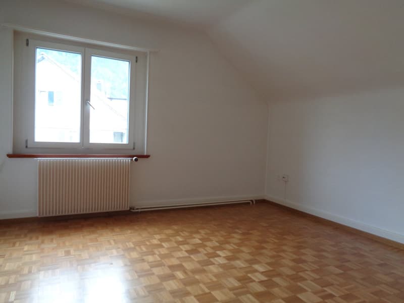 Spacious bedroom with hardwood flooring, white walls, and a large window providing natural light. The room appears to be empty, ready for furnishing and personalization.