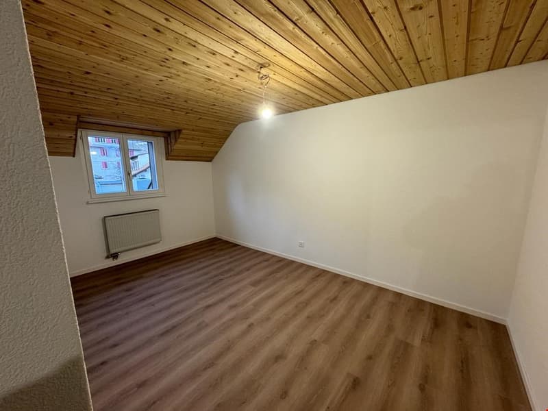 Wooden ceiling, white walls, wooden floor, small window, radiator.