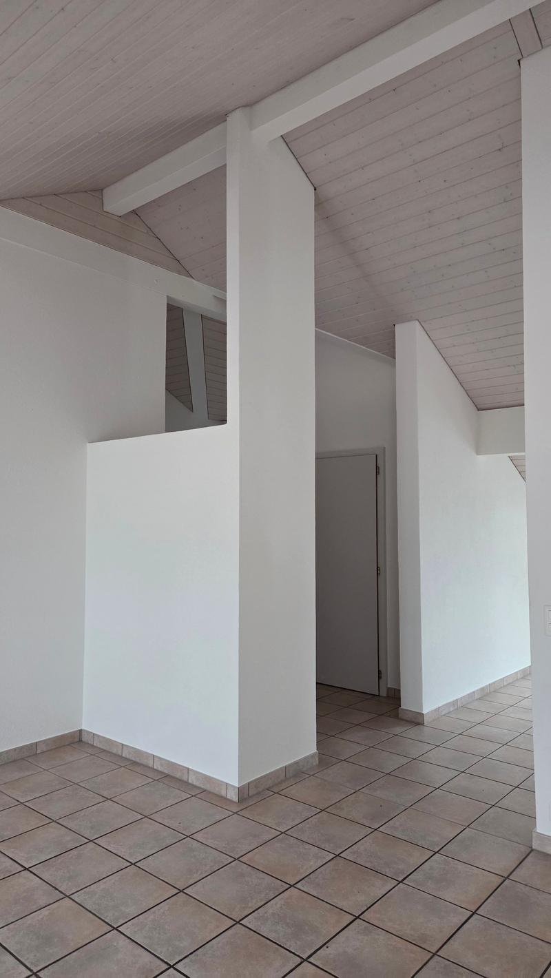 Empty room with white walls, tiled floor, wooden beams on ceiling, doorway.