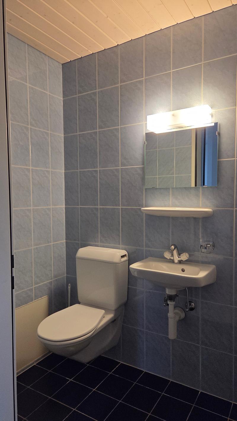 A bathroom with a toilet, sink, and mirror on the wall, tiled floor and wall