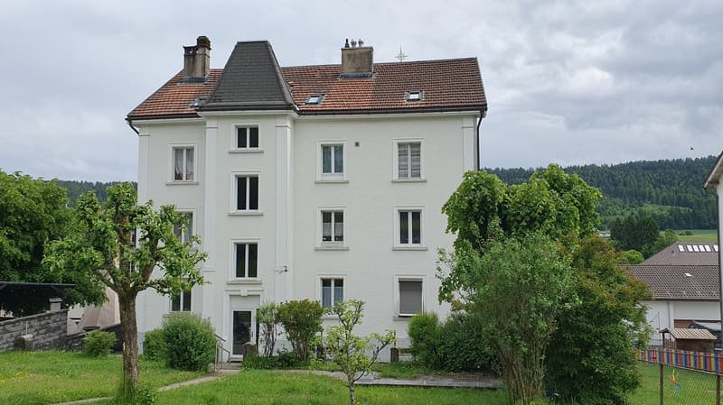 Three story white house, brown roof, chimneys, large windows, garden, trees, small house in the background