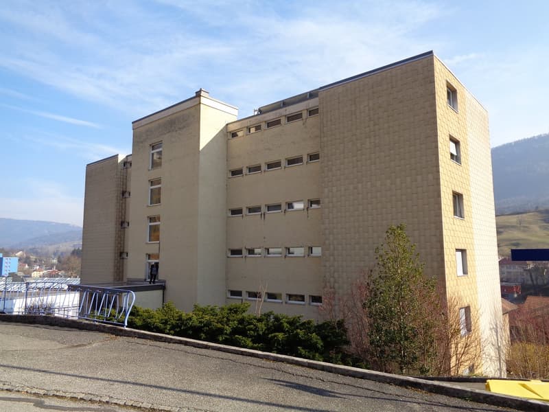 5 story building, brick facade, multiple windows, metal railing on the entrance, surrounding greenery