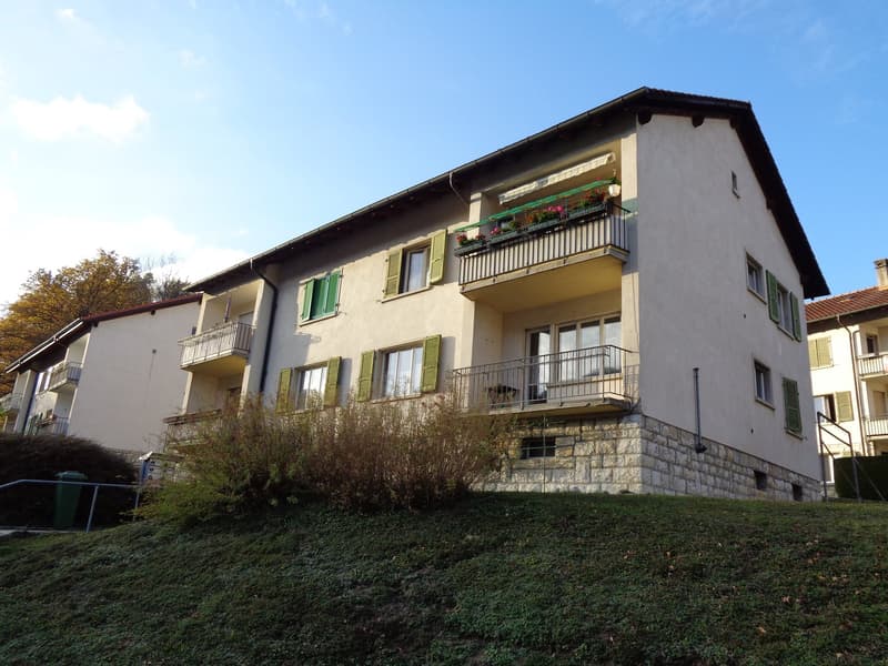 A white stone residential building with balconies, green shutters, and a roof garden