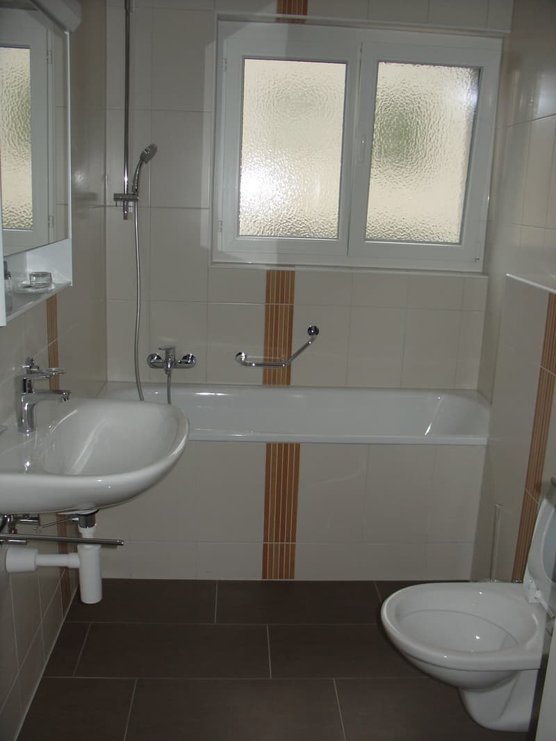 Bathroom with white tiles, bathtub, sink, toilet, shower head, mirror, and a window.