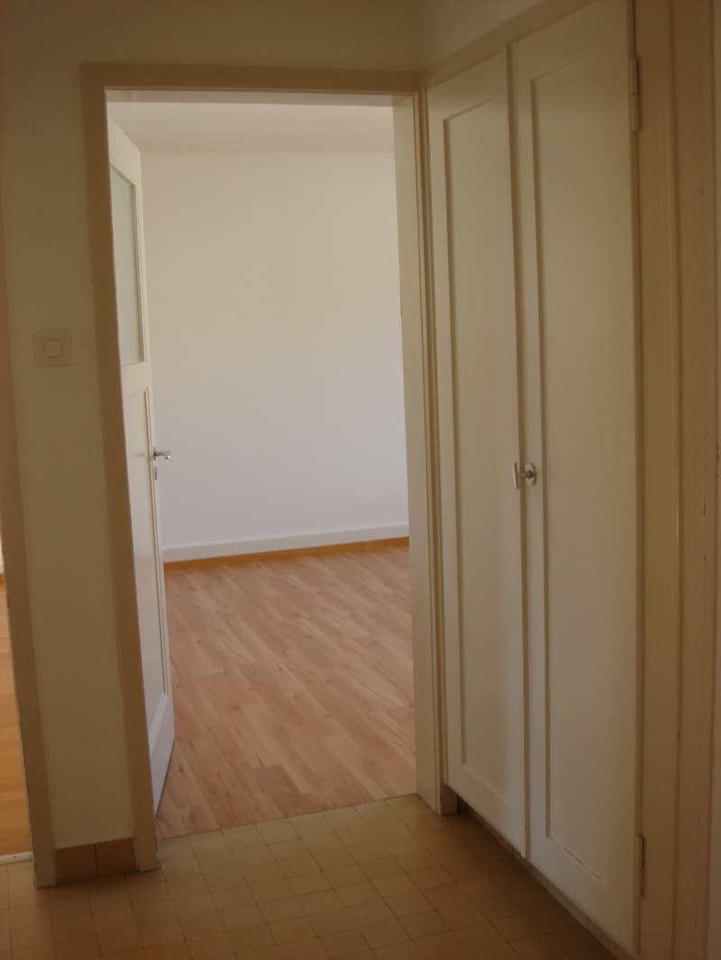 Empty room with wooden floor, white walls, open door, and closet