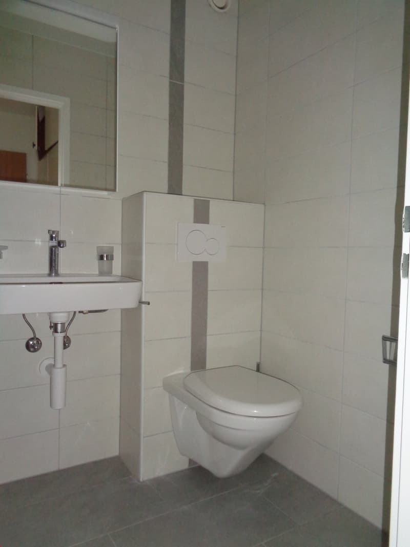 Bathroom with white tiles, white sink, white toilet, mirror, and a small shelf
