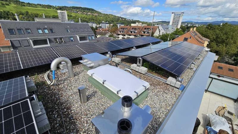 Solar panels, metal structures, gravel surface, distant view of a hill and city buildings