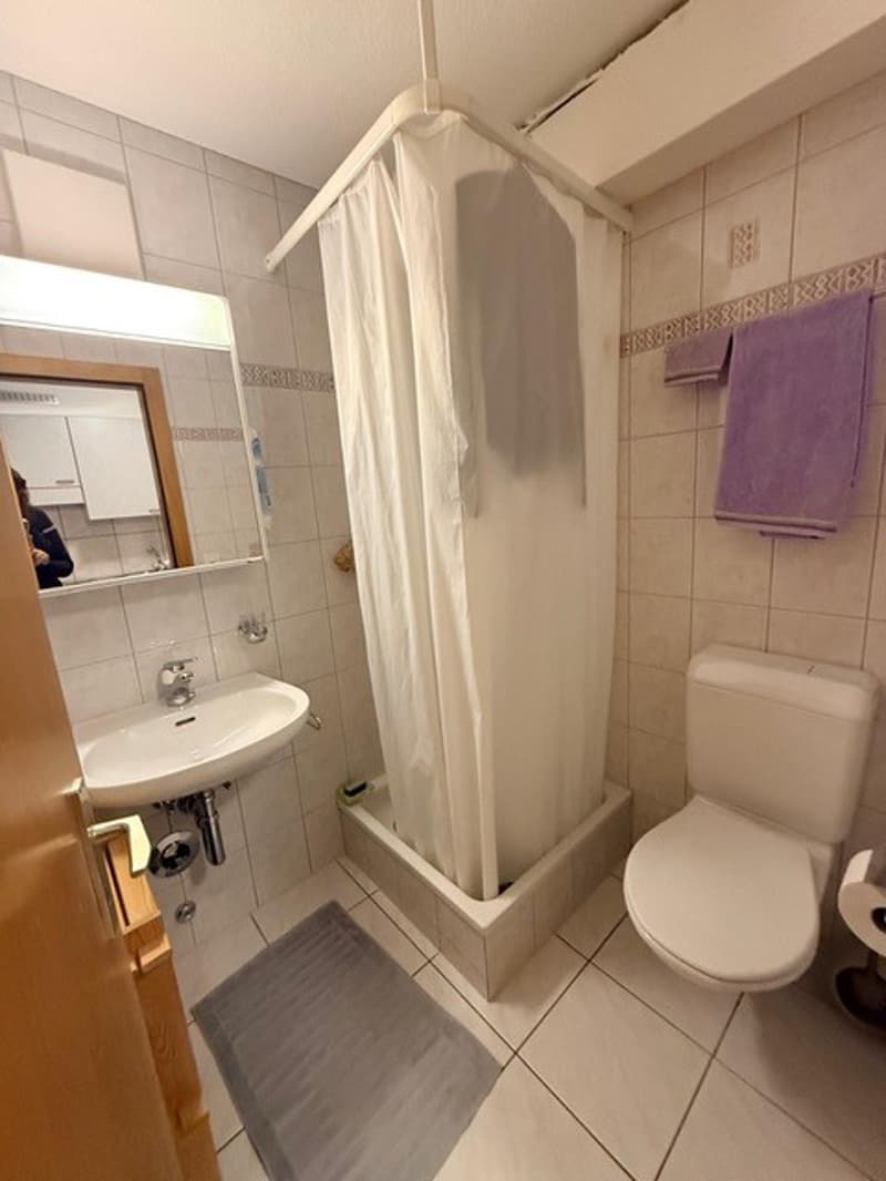 Small white tiled bathroom with shower, sink, and toilet