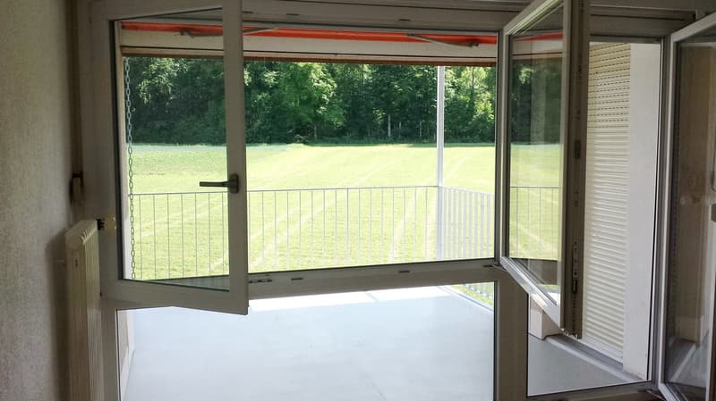 Open balcony doors, fenced balcony, large green field in the distance