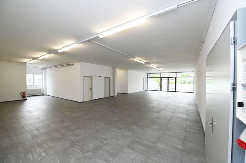 Wide open space, concrete floor, two doors, fire extinguisher, glass walls, white walls, ceiling lights