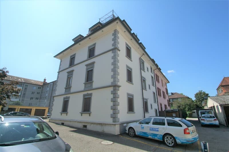 3 story building, white exterior, gray accents, multiple windows, balcony, multiple cars parked