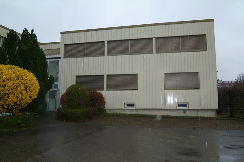2-story commercial building with gray siding, large windows, and a parking area in front