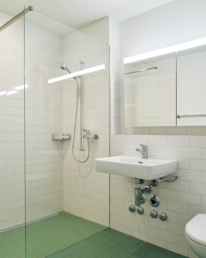 modern bathroom with white tiles, glass shower enclosure, white sink, chrome fixtures, green floor tiles