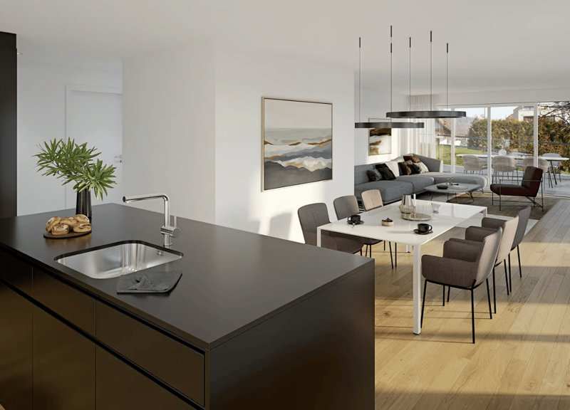 The image shows a modern, open-concept living and dining area. The kitchen features a black countertop and a stainless steel sink. The living room has a large gray sectional sofa, a coffee table, and a framed artwork on the wall. The dining area has a woo