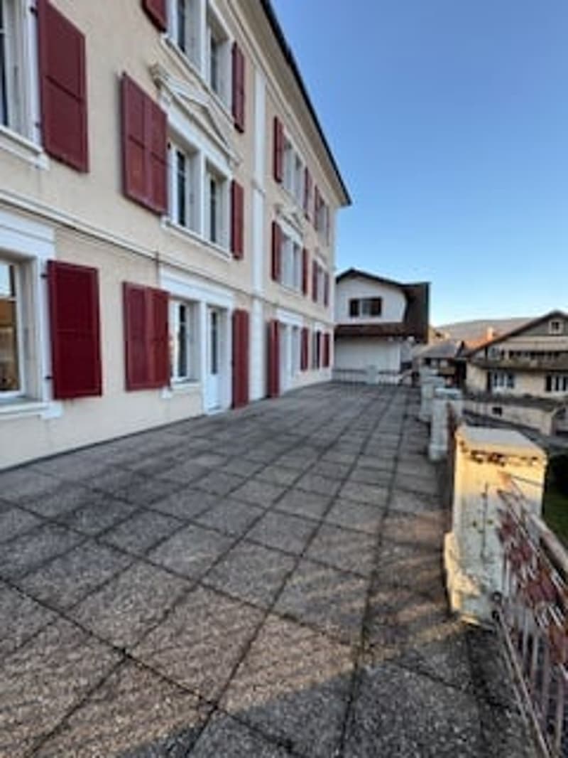 Building with red shutters, paved walkway, balcony, buildings in the background