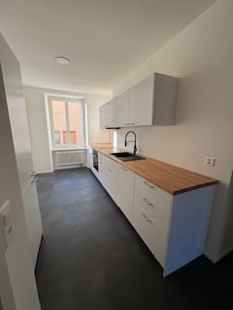 Empty kitchen with white cabinets, wooden countertop, black floor, sink with faucet, window