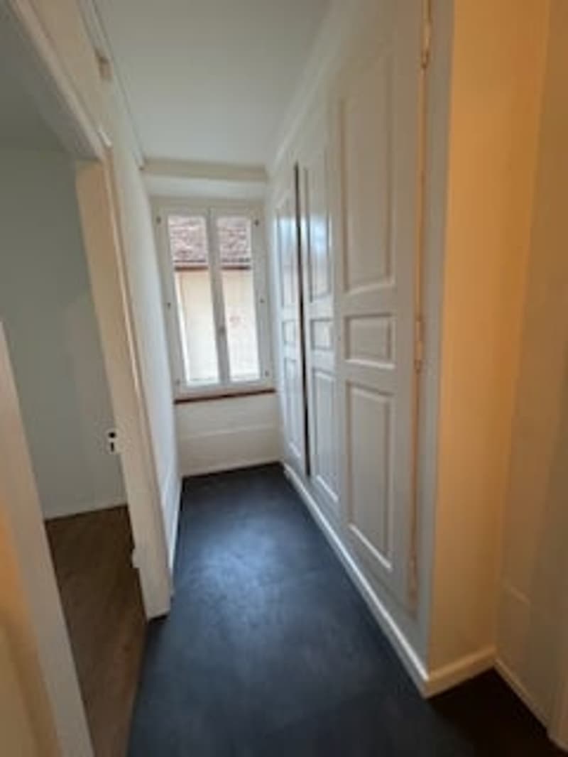 Empty hallway with white walls, black floor, white doors, small window