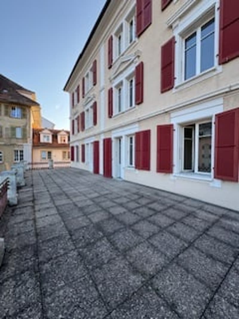 Building with red shutters, white windows, paved courtyard, multiple floors