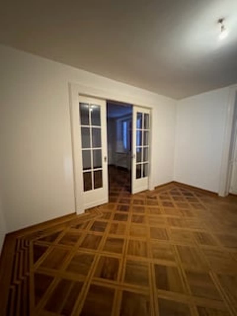Empty room with wooden parquet floor, white walls, two glass doors, and a light on the ceiling