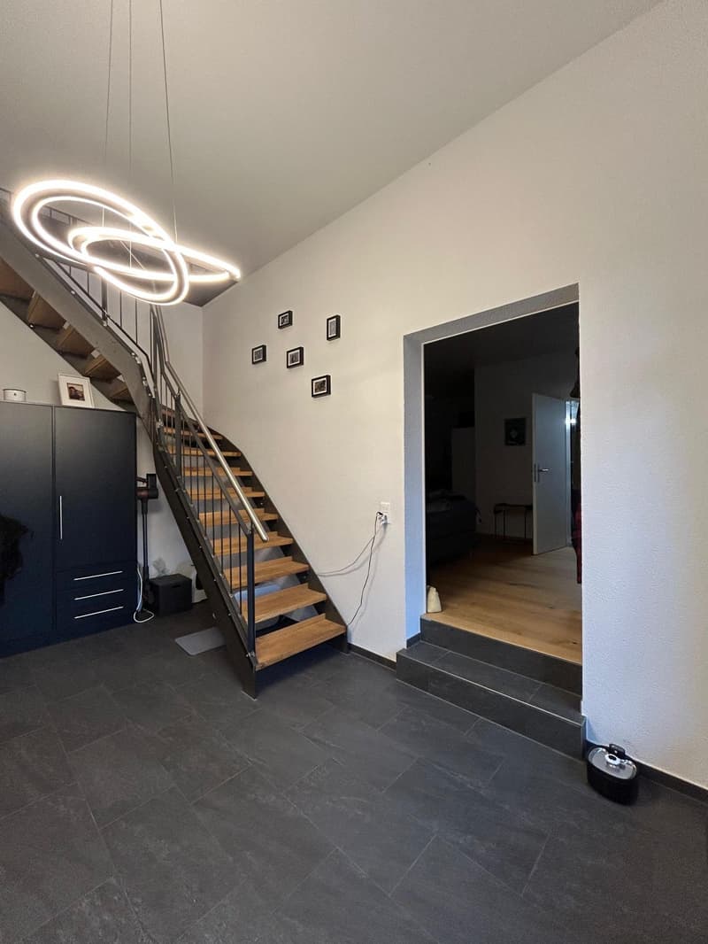 Open staircase, metal handrail, tiled flooring, picture frames, large entrance door, living room visible