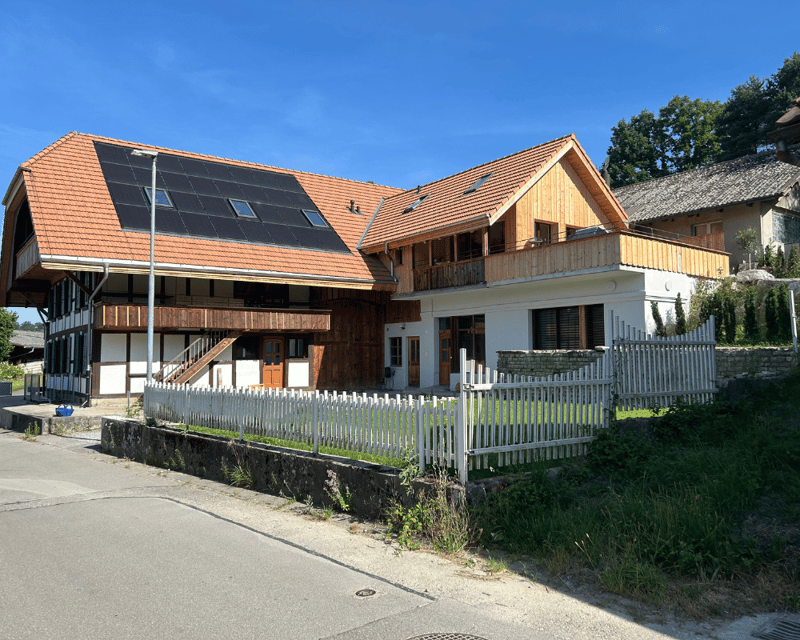 2 story house, wooden facade, red roof, solar panels, white fence, grass yard
