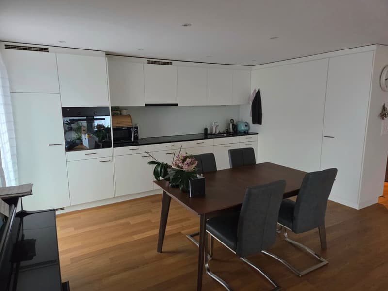modern kitchen with dining area, wooden floor, white cabinets, black countertops, dining table with 4 chairs, microwave, sink, flower vase, piano