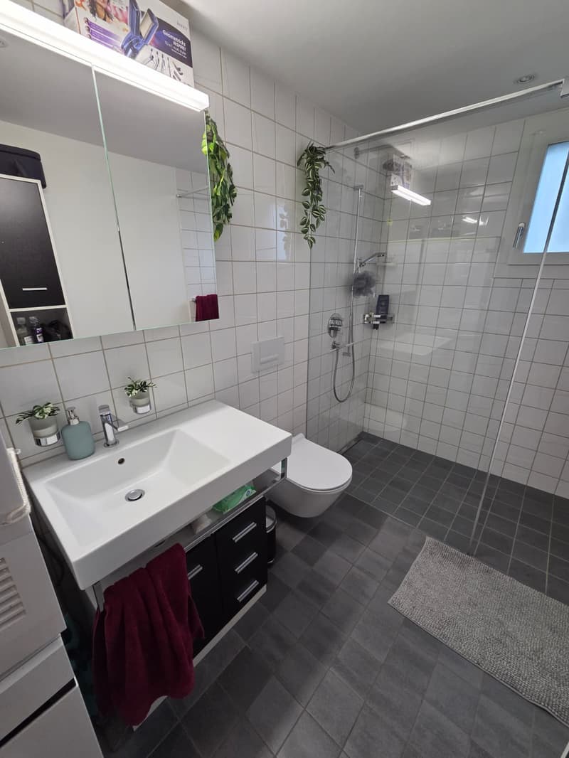 modern bathroom with white tiles, white sink, white toilet, glass shower enclosure, towel hanging on rack