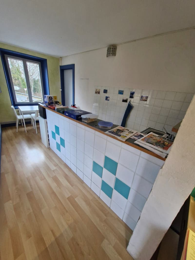 Empty room with wooden floor, white tiled wall, window, countertop, and desk.