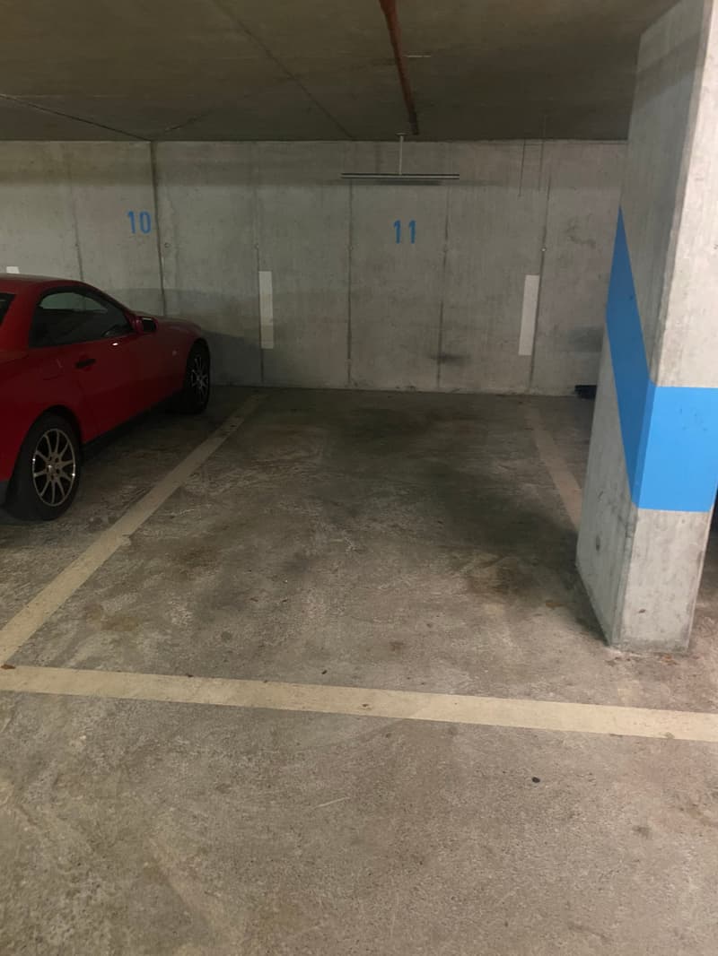 concrete floor, two doors on the wall with numbers, red car parked, empty parking area